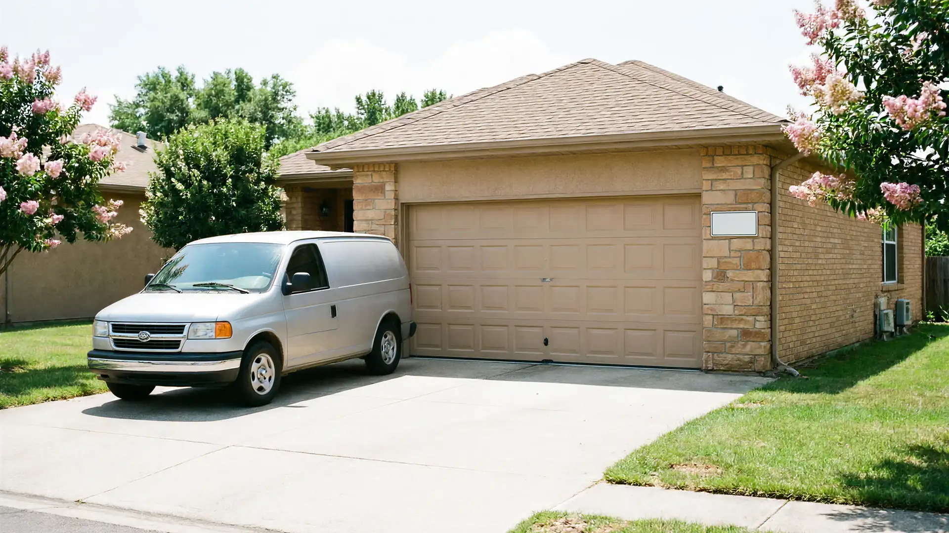 A silver van is parked in the driveway of a house with a tan garage door.