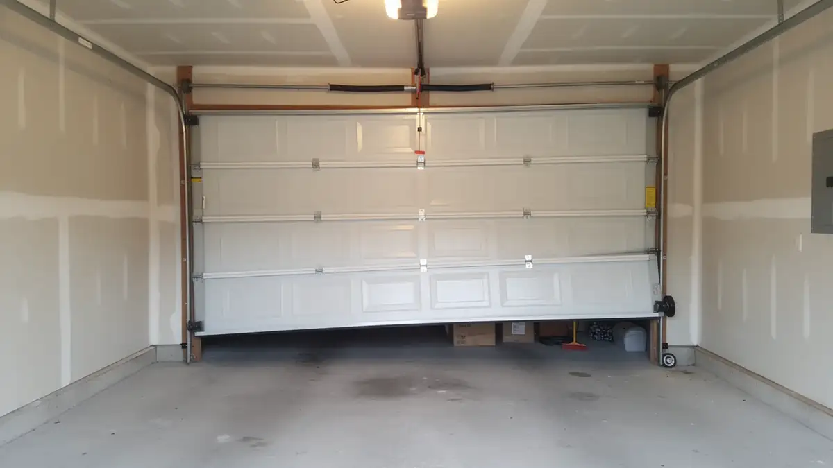 A white garage door is off its tracks and crooked in a garage.